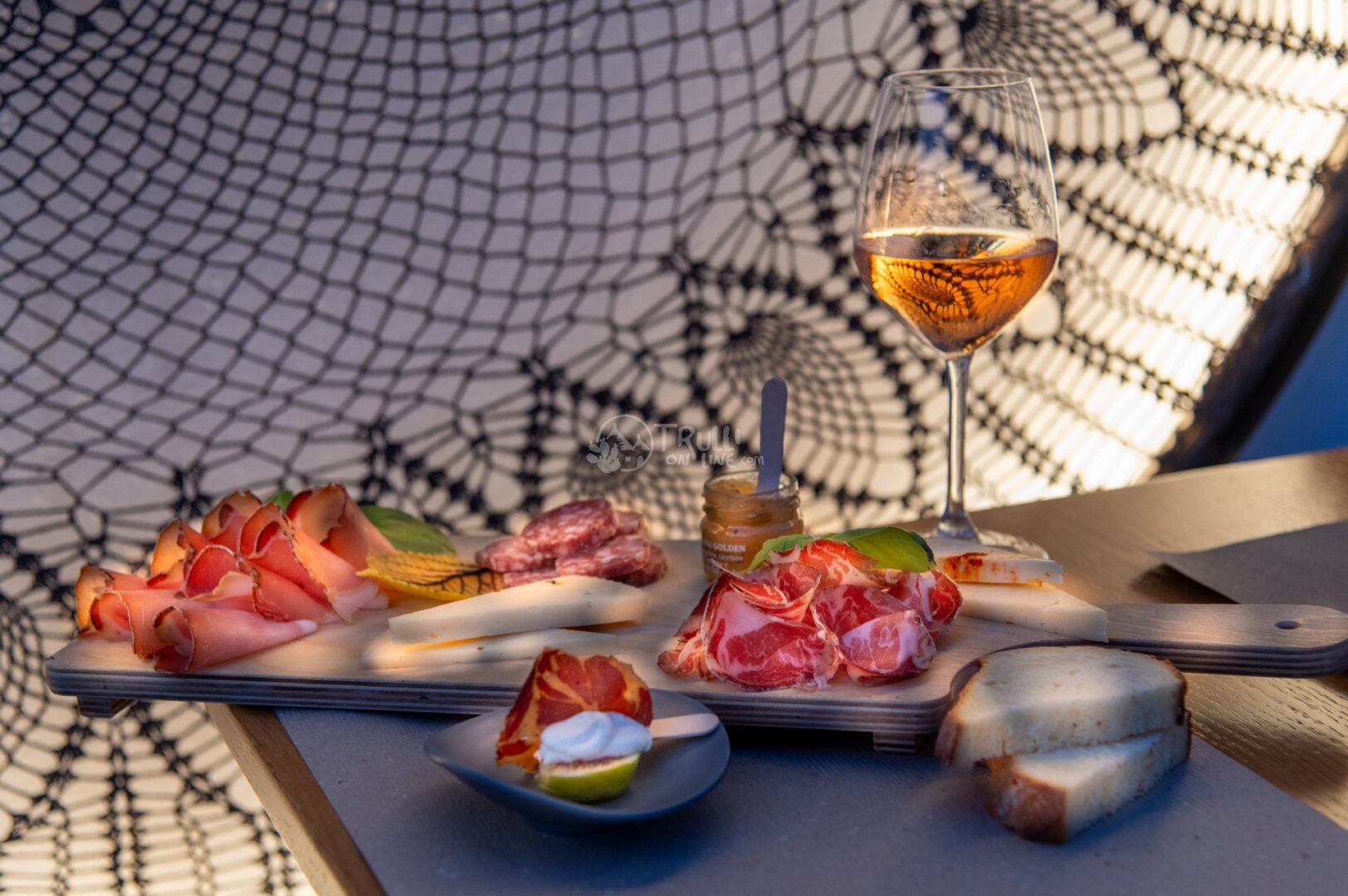 guida-cisternino-trullionline-01 Tagliere di salumi e formaggi con miele e un calice di vino rosato su un tavolino