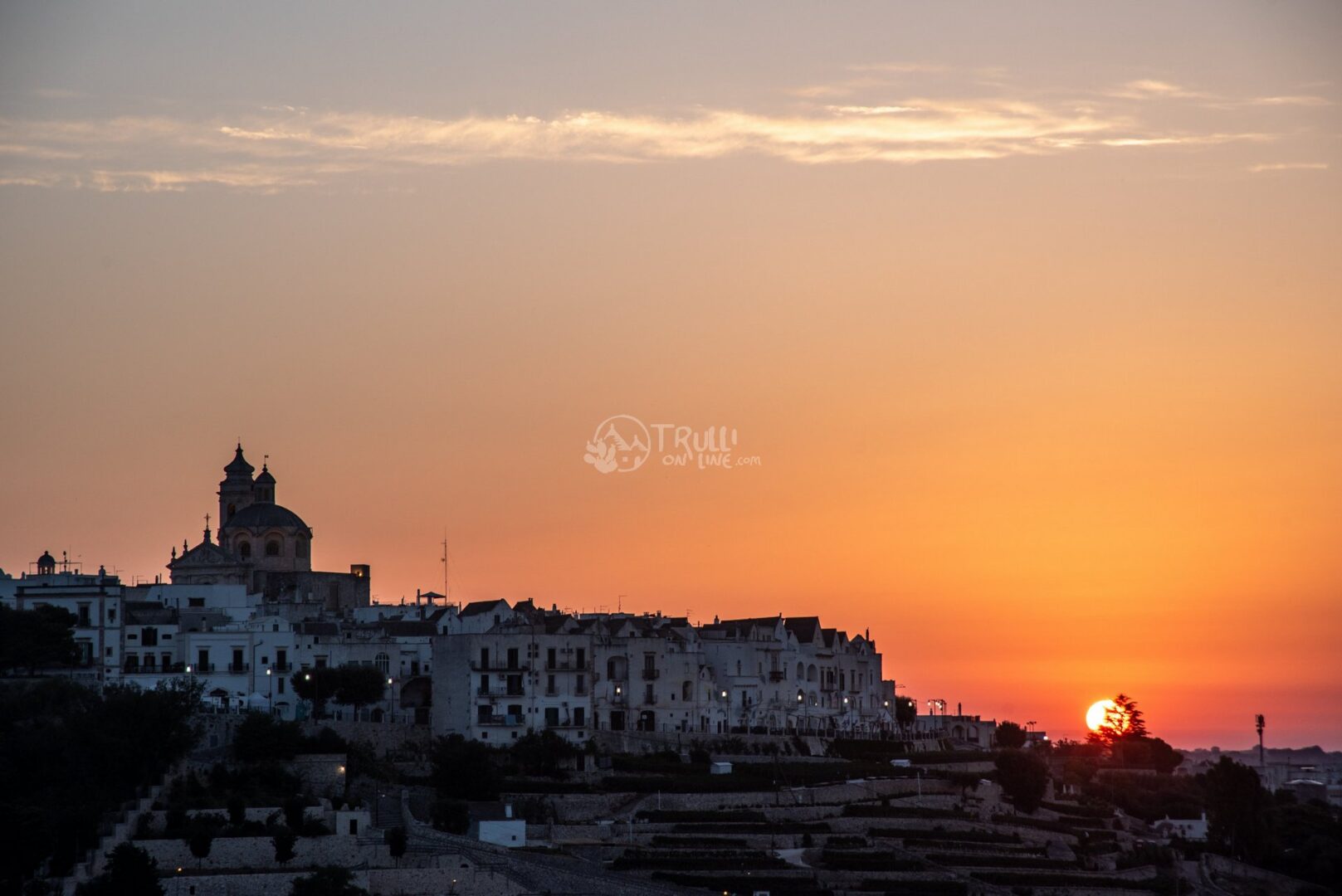 Sagoma del paese sulla collina con una chiesa a cupola, contro il cielo arancione del tramonto