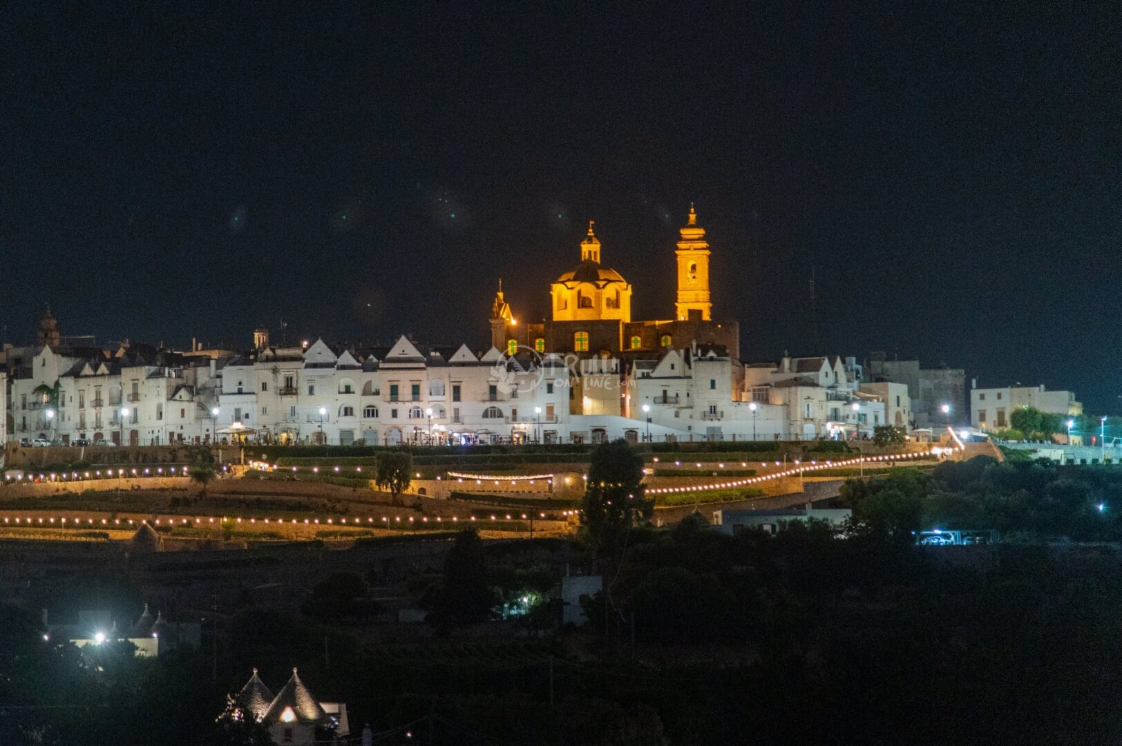 Il paese sulla collina illuminato di notte, con la chiesa a cupola in luce dorata e file di luminarie