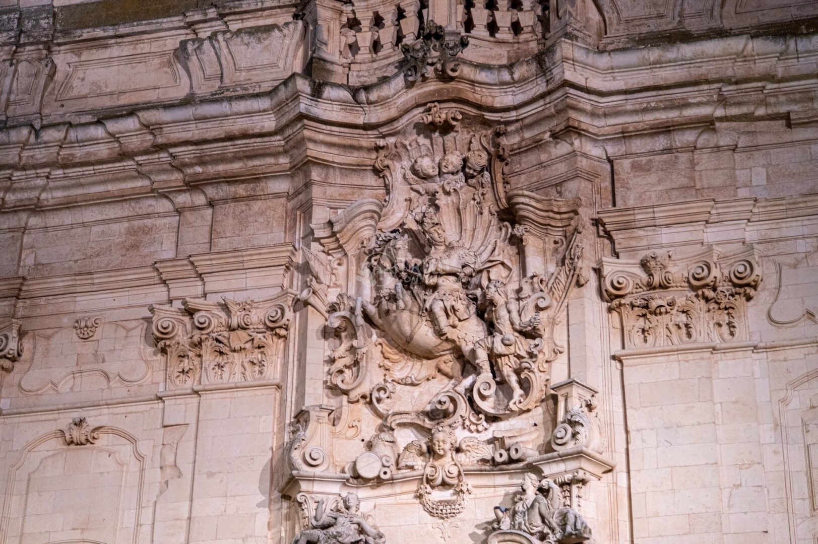 guida-martina-trullionline-05 Dettaglio scolpito della facciata di una chiesa barocca illuminata di notte, con statue e decorazioni
