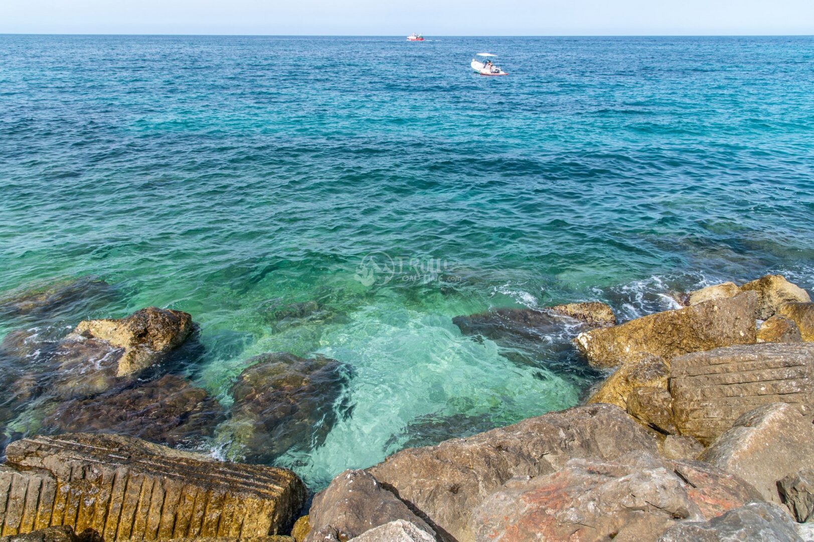 guida-savelletri-e-torrecanne-trullionline-06 Mare turchese e trasparente tra grandi scogli, con una barca in lontananza