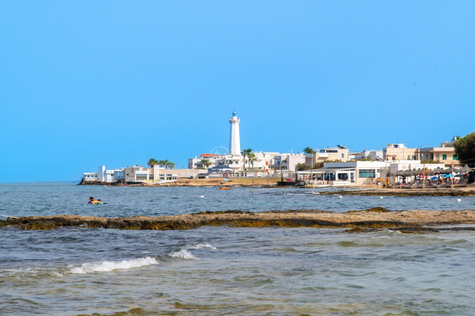 guida-savelletri-e-torrecanne-trullionline-26 La costa vista dagli scogli, con il faro e le case bianche sul litorale